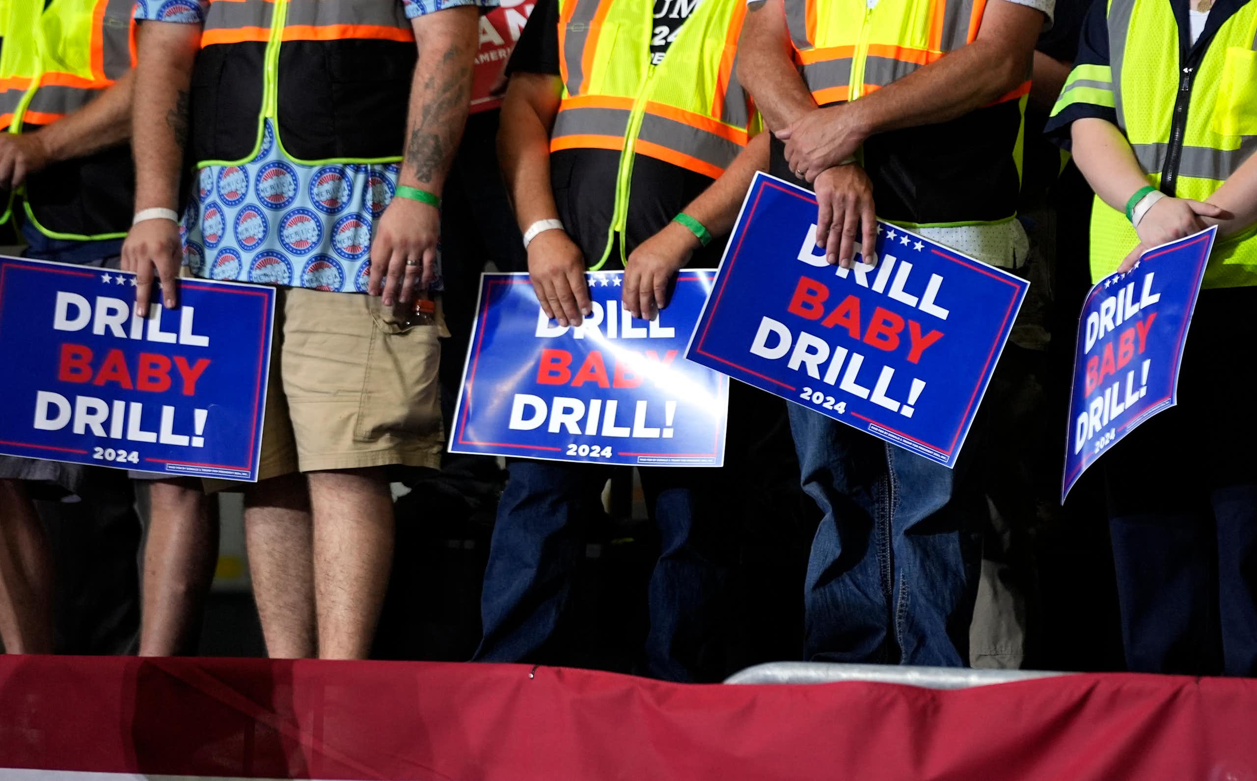 People stand in a row carrying placards that read: drill baby drill