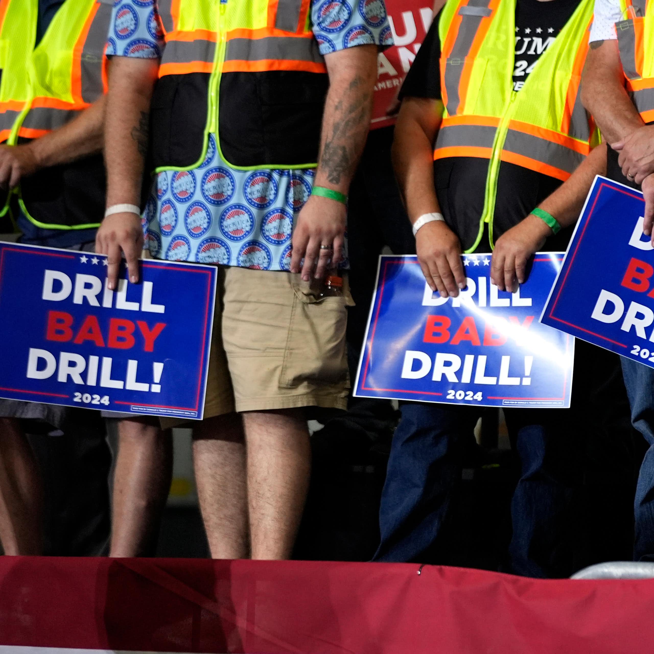 People stand in a row carrying placards that read: drill baby drill