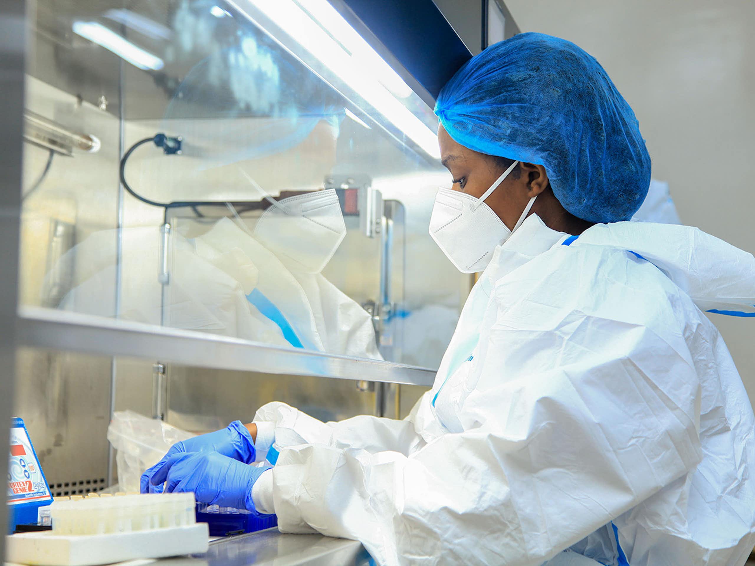 Woman in laboratory, dressed in protective cap, face mask, overall and gloves 