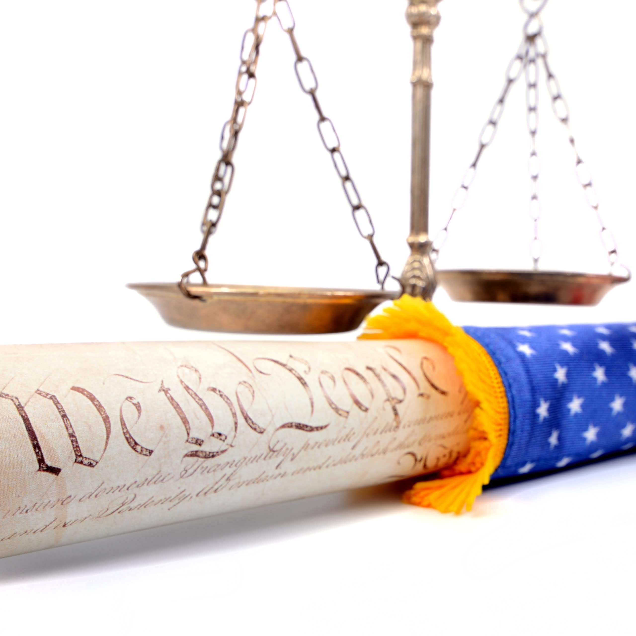 A copy of the Constitution is rolled into a US flag and in front of scales.