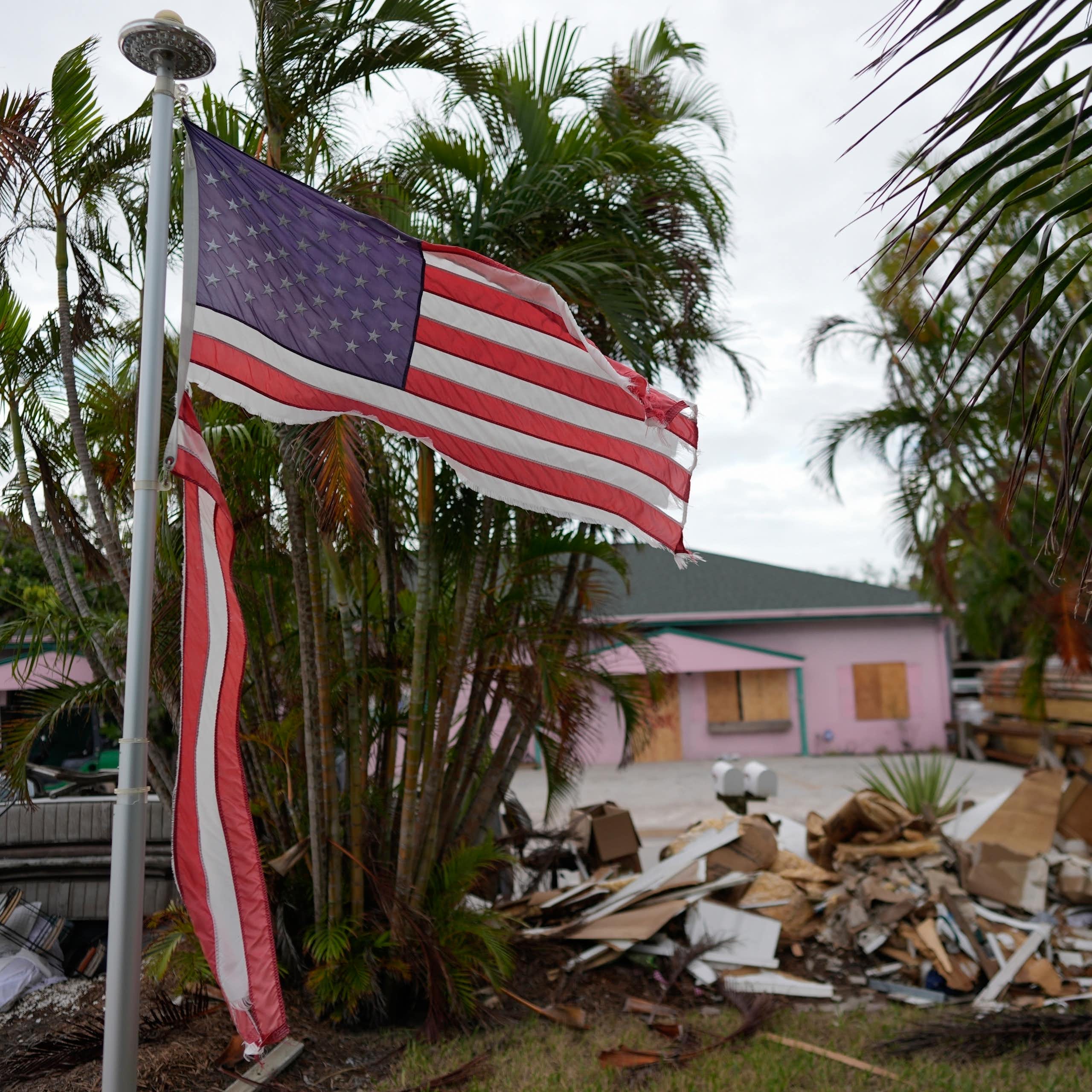a tattered American flag flaps outside a home with furniture and household items damaged